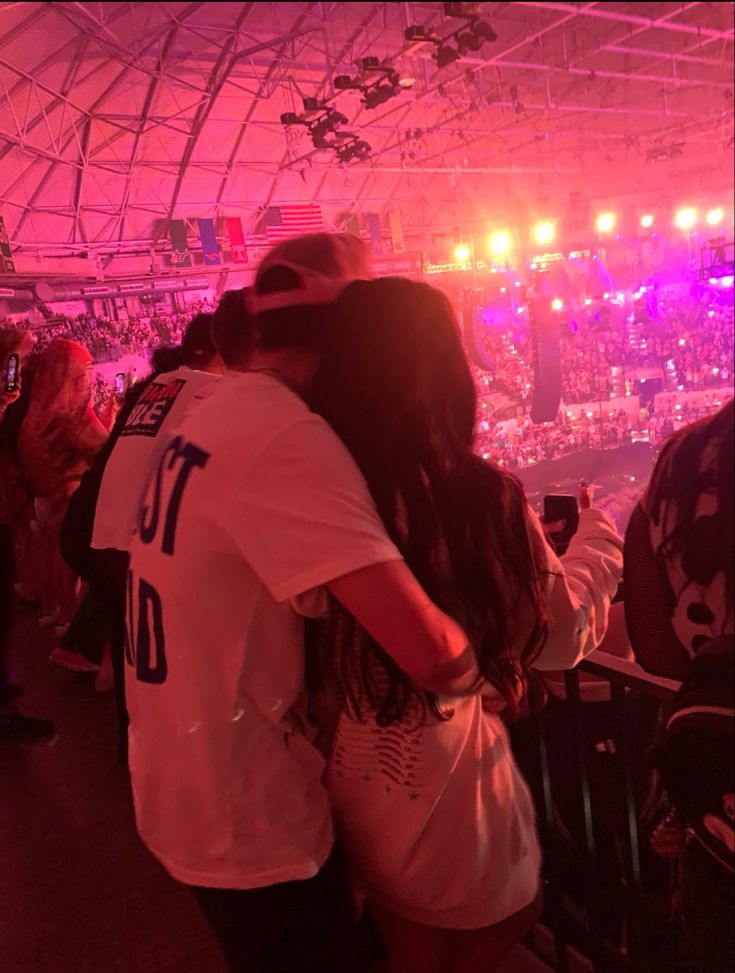 two people embracing each other in front of an audience at a concert with bright lights