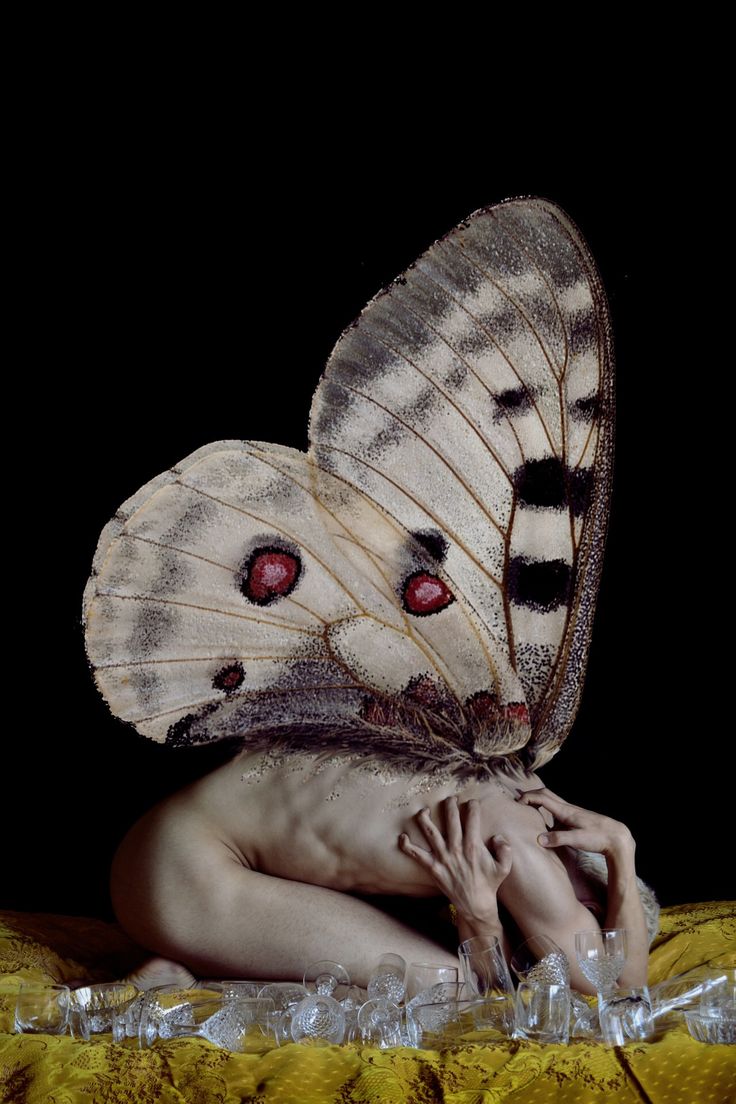 a naked woman with large butterfly wings on her head and body, sitting in front of a black background