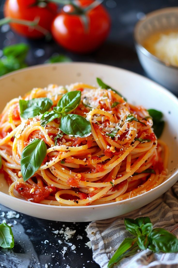 a plate of spaghetti with tomato sauce and basil on the table next to some tomatoes