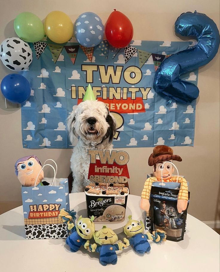 a dog is sitting in front of two birthday decorations and balloons on the table with his head down