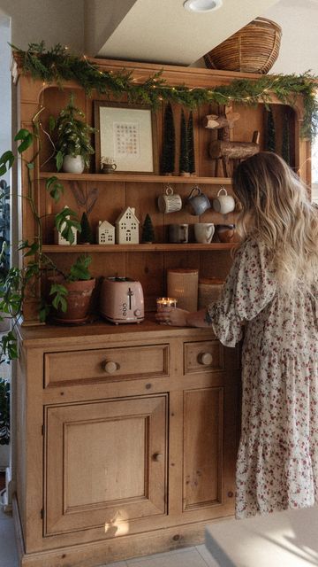 a woman standing in front of a wooden cabinet filled with plants and potted plants