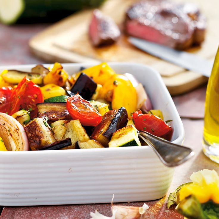 a white bowl filled with assorted vegetables next to a glass of beer