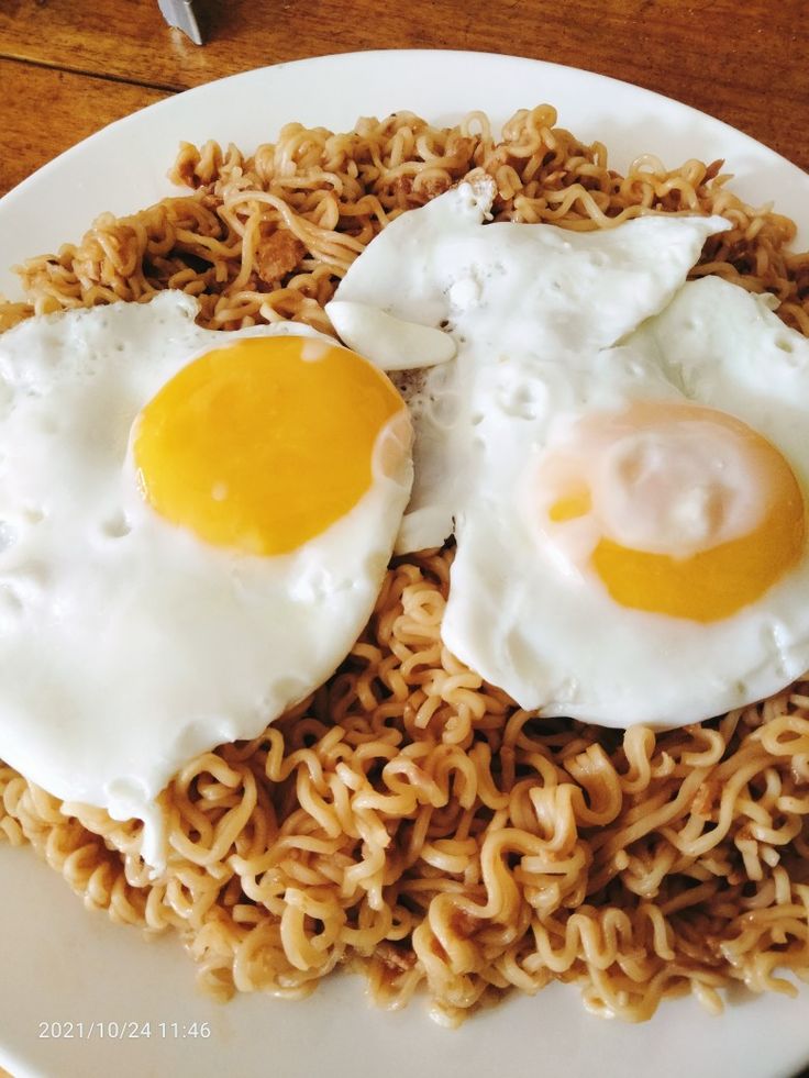 two fried eggs are on top of noodles