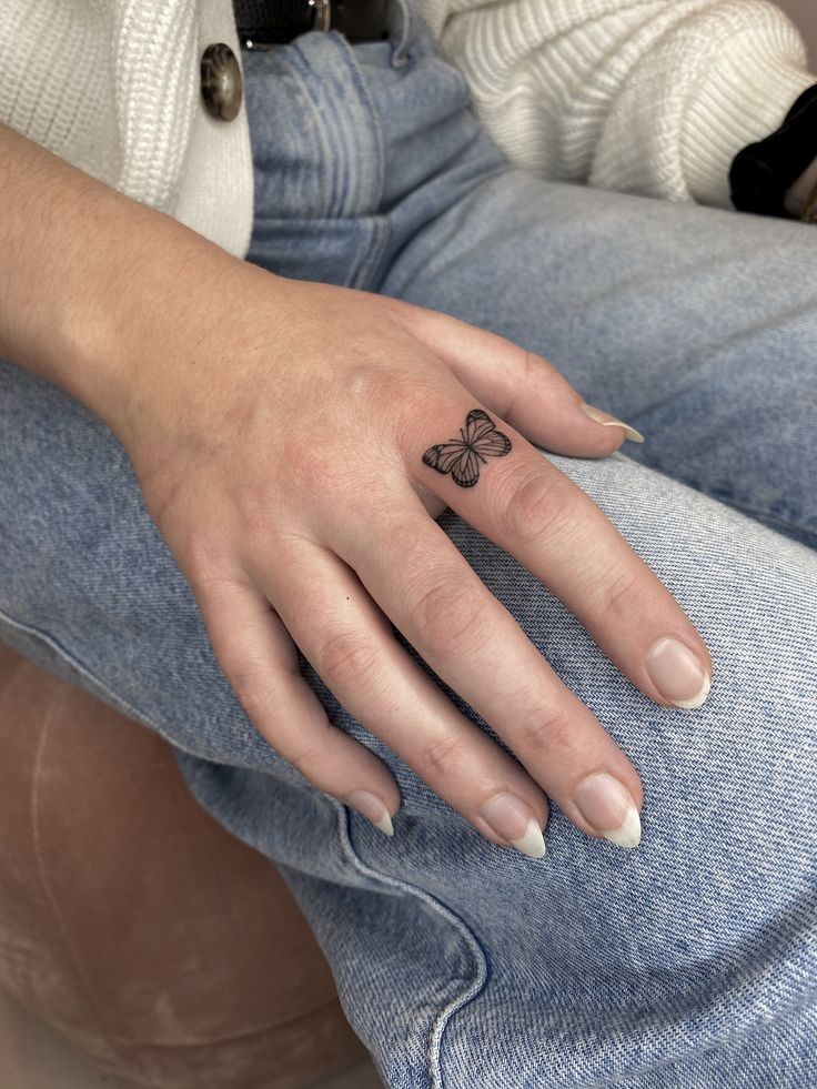 a woman's hand with a small butterfly tattoo on her left thumb and finger