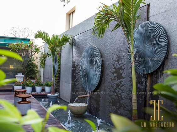 an outdoor water feature with plants and potted trees in the background, surrounded by concrete walls