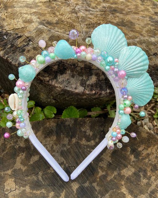 a headband with seashells and pearls on it sitting on a piece of wood