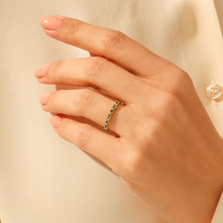 a woman's hand wearing a gold ring with green stones on it and a pearl necklace