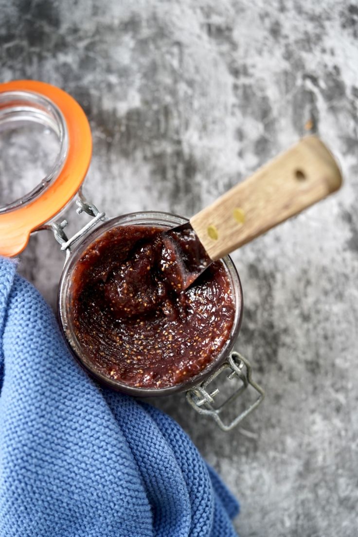 a jar filled with food sitting on top of a blue towel next to a wooden spoon