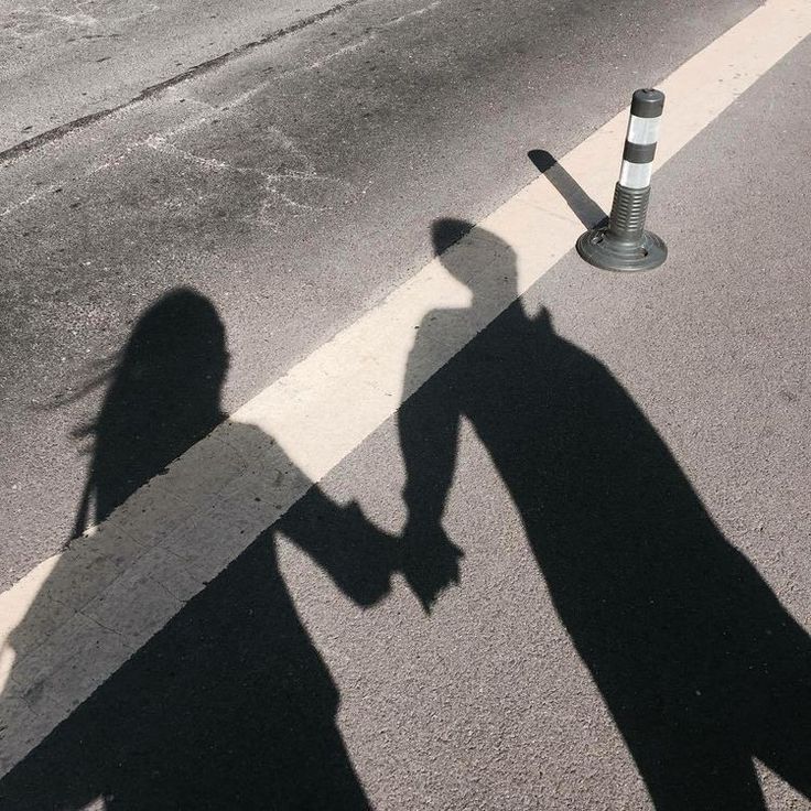 the shadow of two people holding hands next to a traffic cone on a street corner