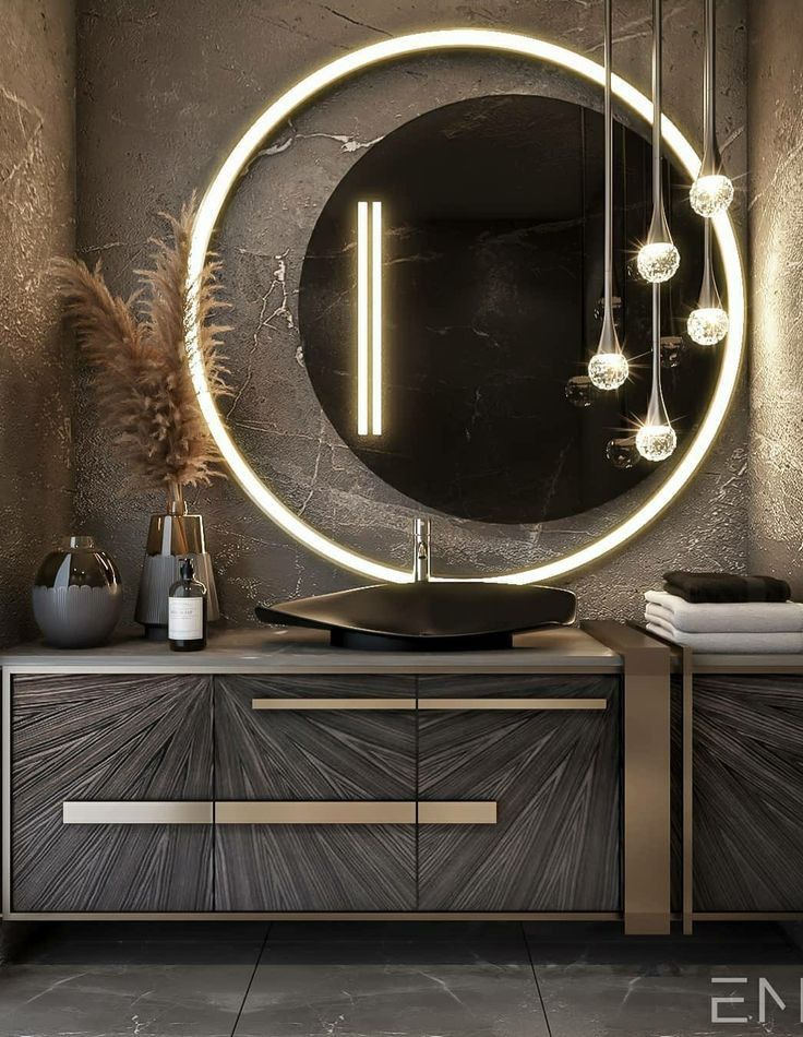 a bathroom vanity with a round mirror and lights on the wall above it, along with two vases