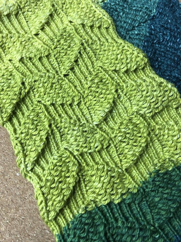 a green and blue knitted blanket sitting on top of a floor next to a rug