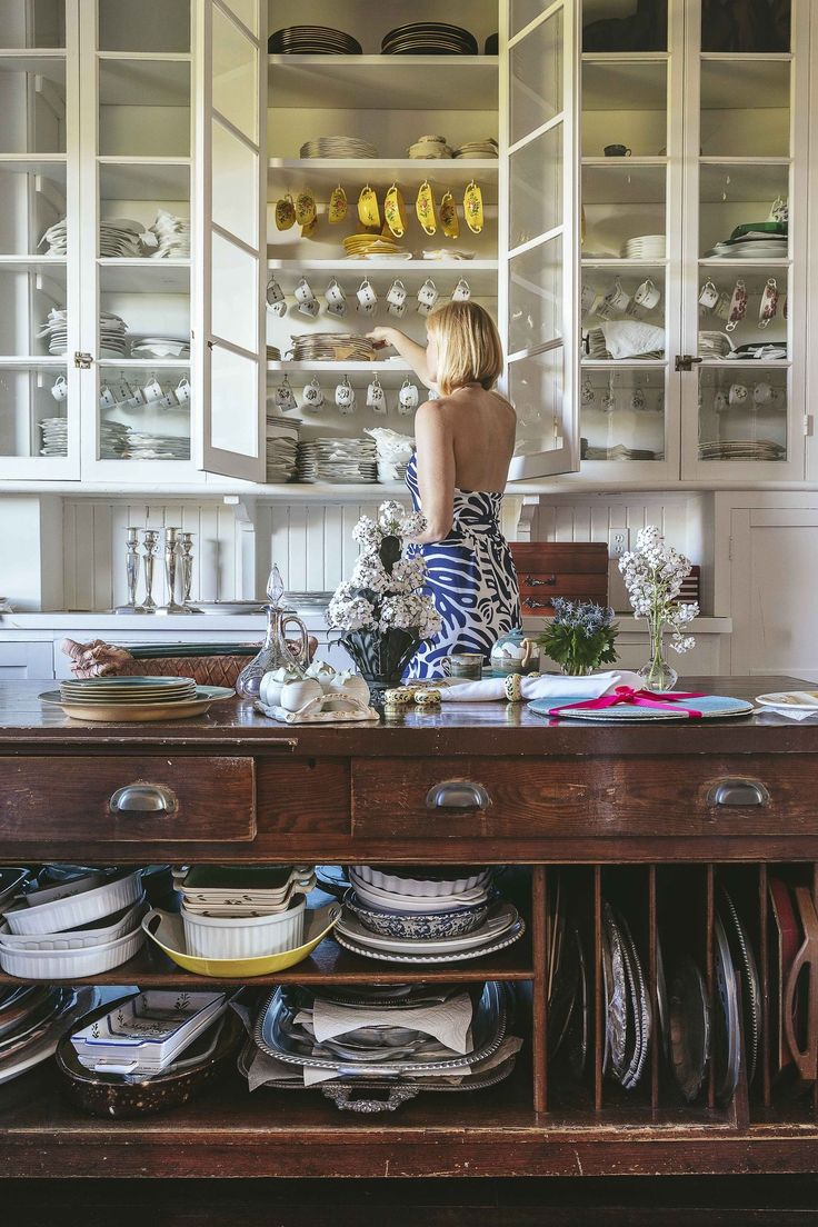 a woman standing in front of a wooden table filled with dishes