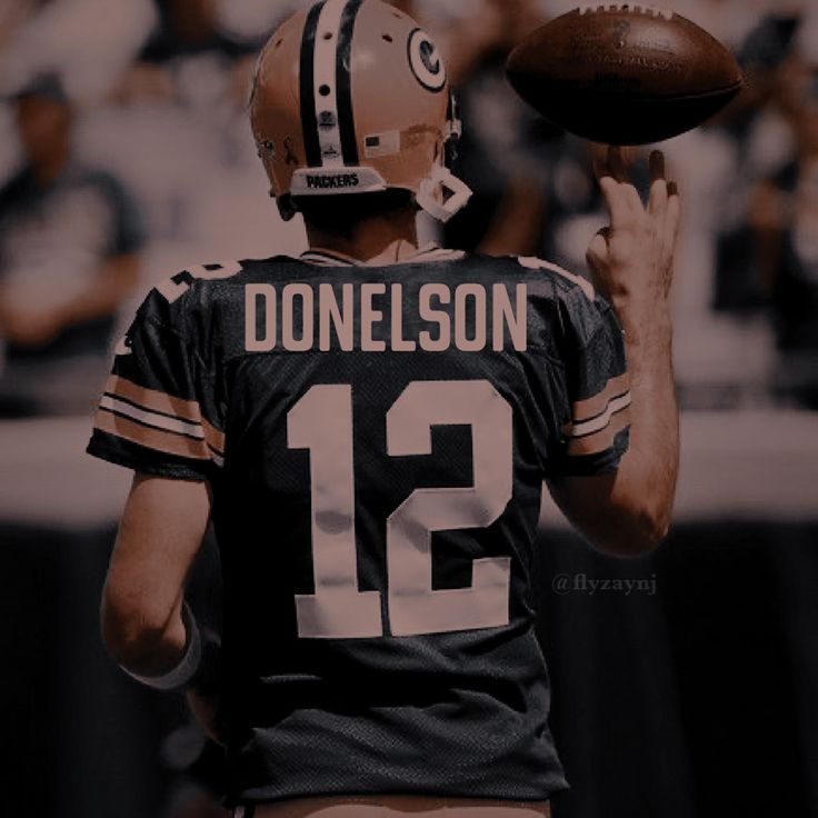 a man holding a football in his right hand and wearing a jersey with the number 12 on it