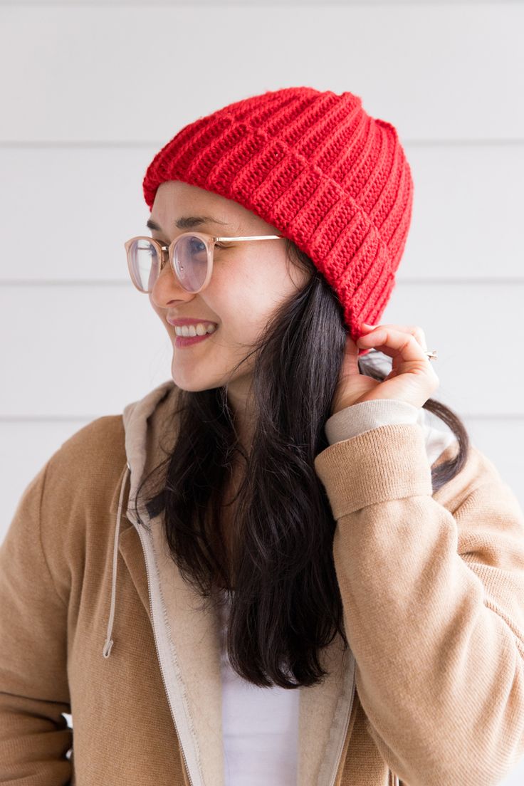 a woman wearing a red knitted hat while holding her hair in one hand and looking to the side