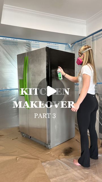 a woman in black pants and white shirt spray painting a silver refrigerator with green paint