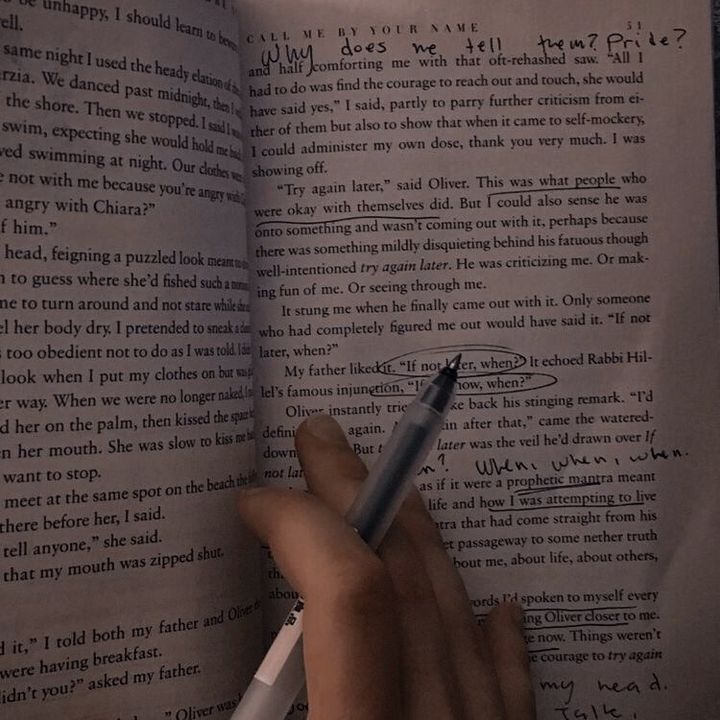 a hand holding a pen over an open book with writing on the pages in it