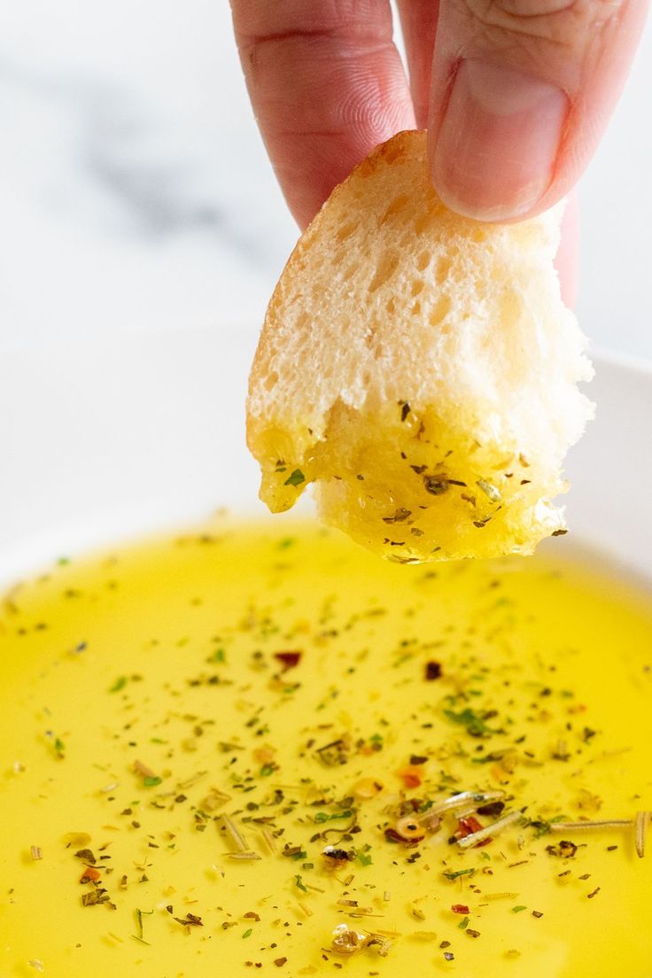 a hand holding a piece of bread over a bowl of soup with mustard in it