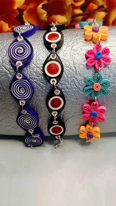 three different colored bracelets sitting on top of a silver object with flowers in the background