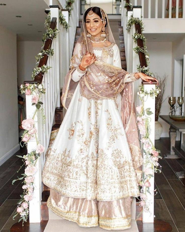 a woman in a white and gold bridal gown standing on stairs with flowers around her