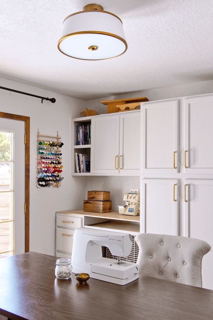 a sewing machine sitting on top of a wooden table in front of white cabinets and drawers