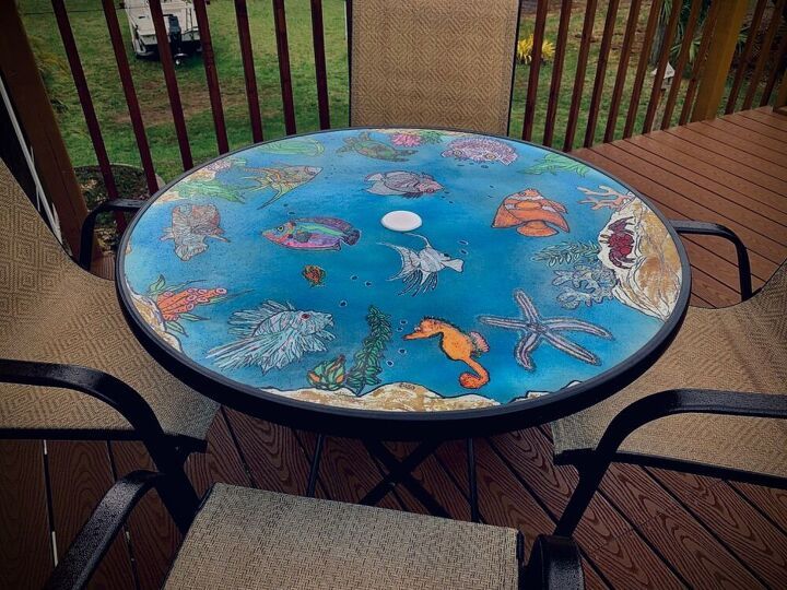 an outdoor table with fish painted on it and two chairs sitting in front of it