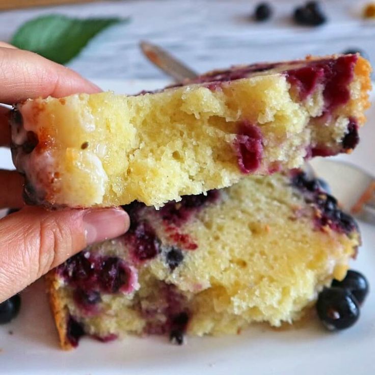 two pieces of cake with blueberries on it being held by someone's hand