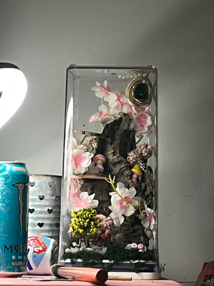 a glass case with flowers and rocks in it sitting on a table next to cans