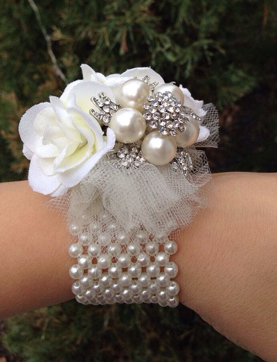 a white wrist corsage with pearls and flowers on it's arm,