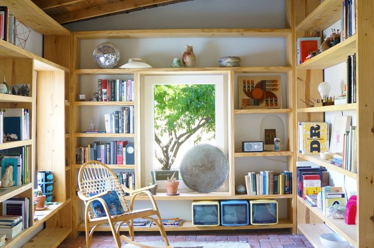 a room filled with lots of books and furniture next to a window on top of a hard wood floor