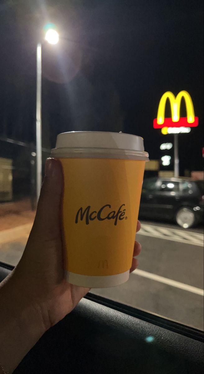 a person holding up a cup of coffee in front of a mcdonald's sign