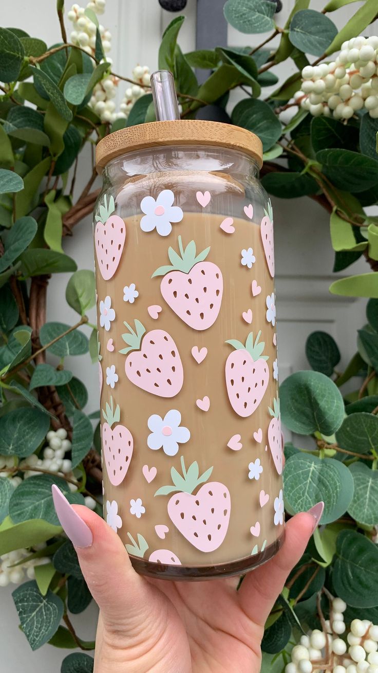 a hand holding a mason jar with strawberries on it and flowers in the background