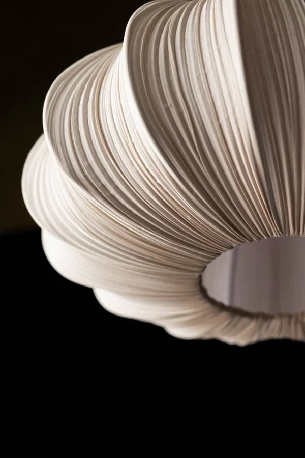 a close up of a light fixture made out of white paper and wood strips on a black background