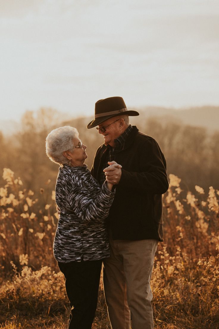 an older man and woman dancing together in a field with tall grass on the other side