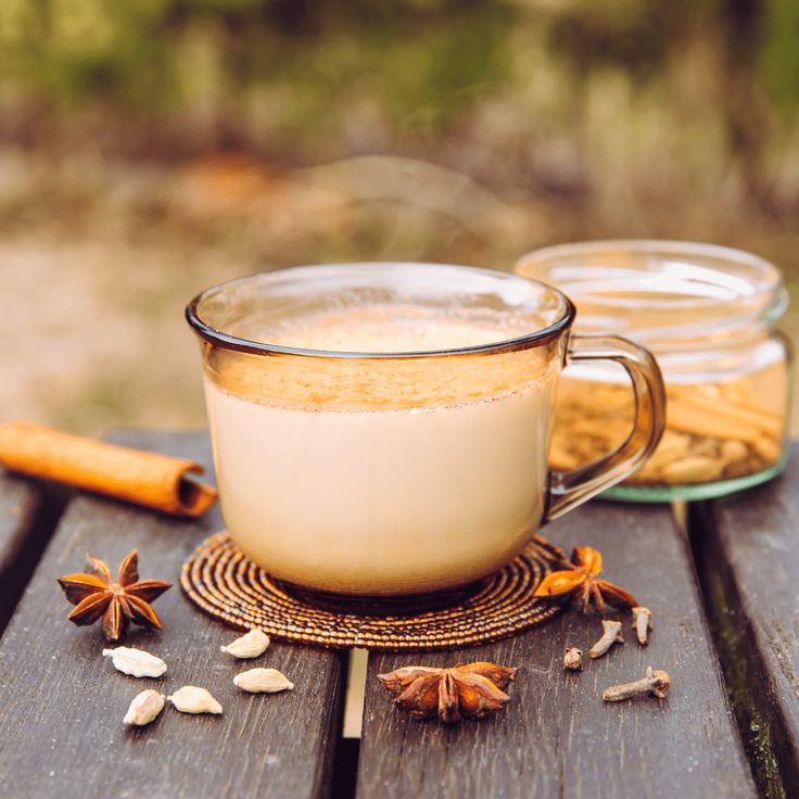 two mugs filled with liquid sitting on top of a wooden table next to cinnamon sticks