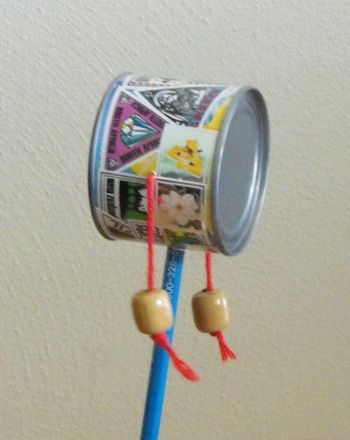 a person holding up a tin can with stickers on it's sides and two bells attached to the top