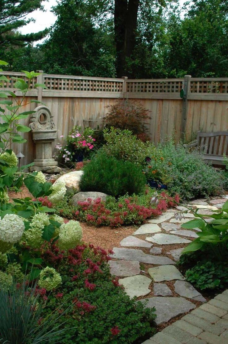 a garden with lots of flowers and plants around it, along with a bench in the middle