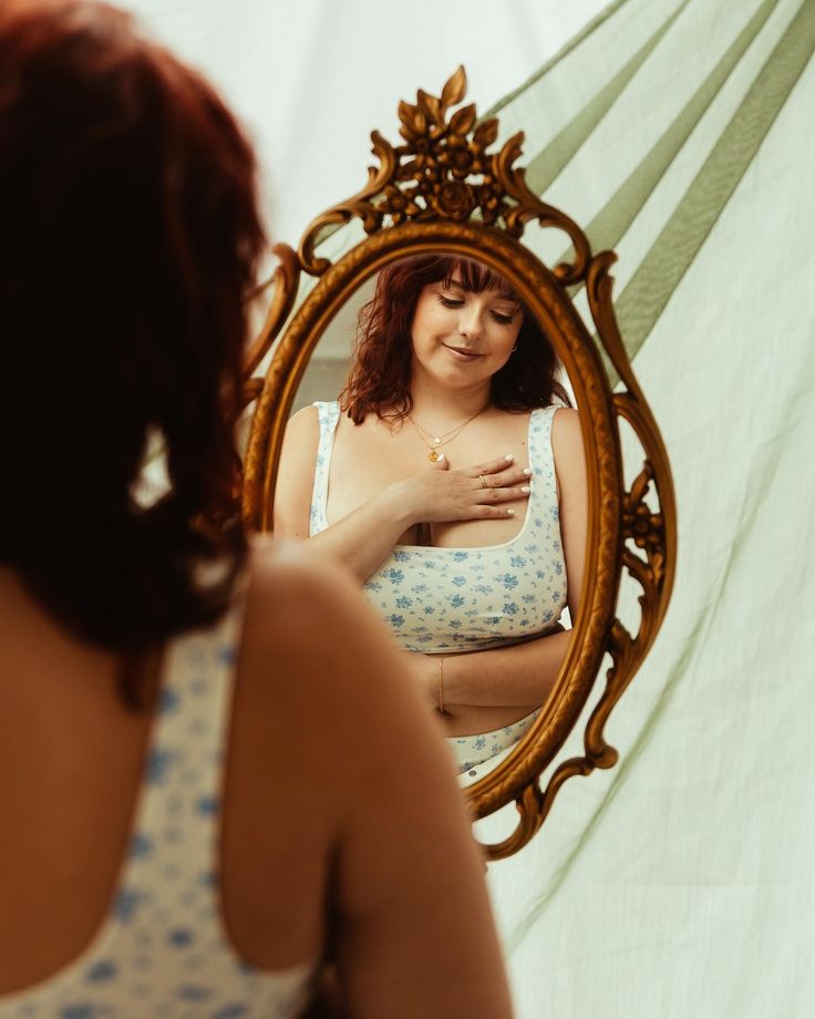 a woman looking at her stomach in front of a mirror with the reflection of herself