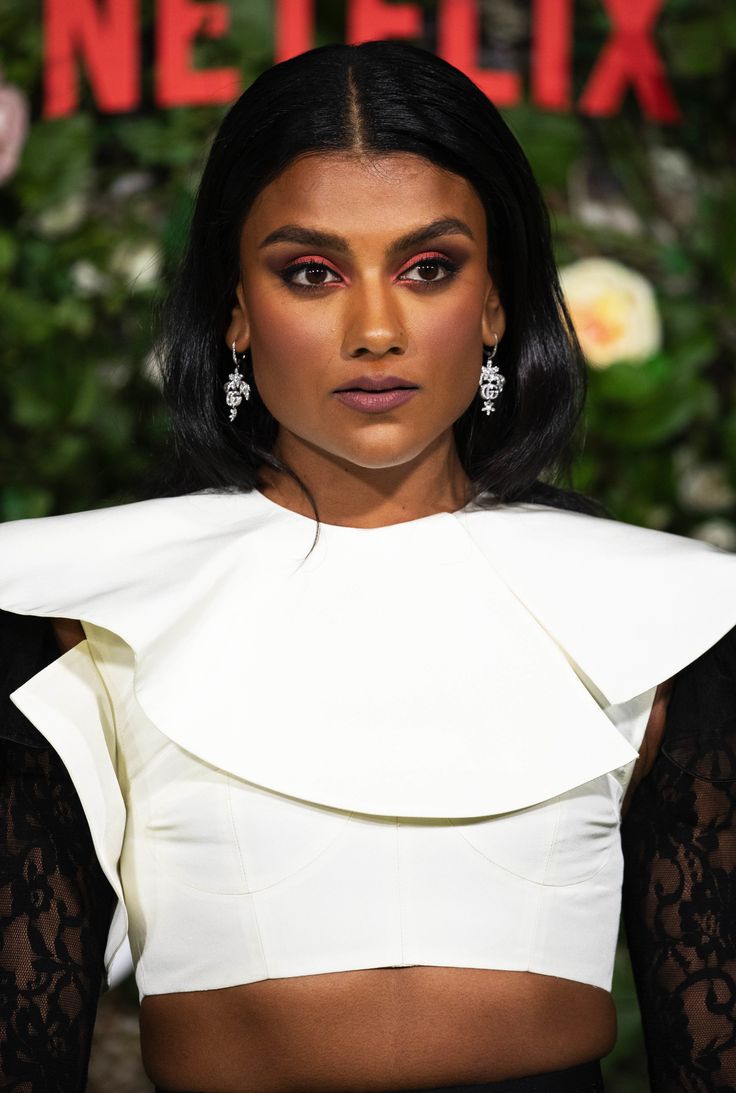 a woman with dark hair wearing a white top and black skirt