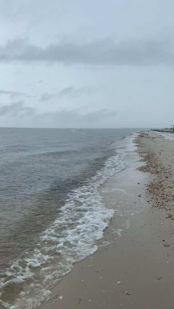 an empty beach next to the ocean under a cloudy sky