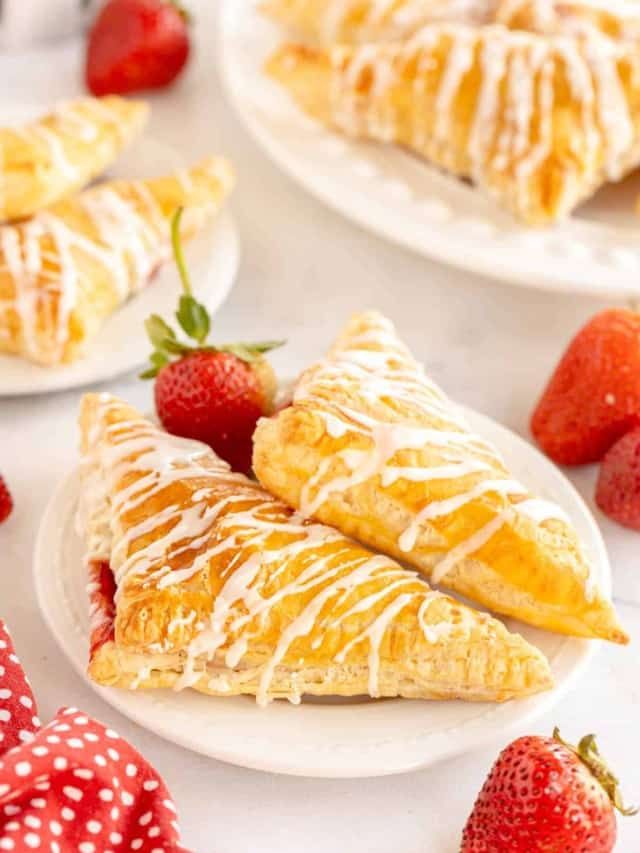 strawberry turnovers with icing and strawberries on white plates next to other pastries