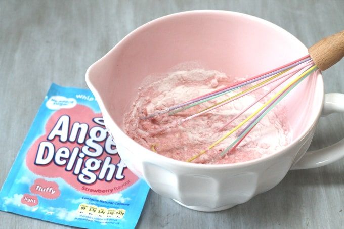 a bowl filled with pink ice cream next to a packet of angel delights on a table