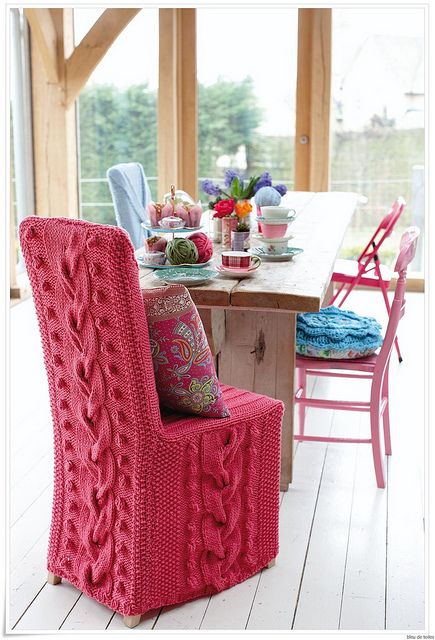 a bright pink chair sits in front of a table with colorful pillows and blankets on it