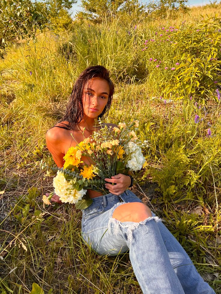 a woman sitting on the ground with flowers in her hand and looking at the camera