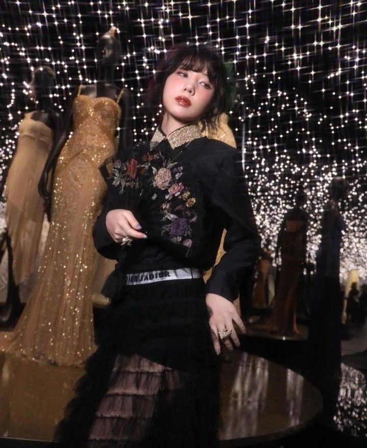 a woman standing in front of mannequins with lights on the wall behind her