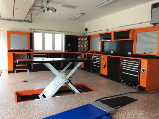 an orange and black workbench in a garage with tools on the floor next to it