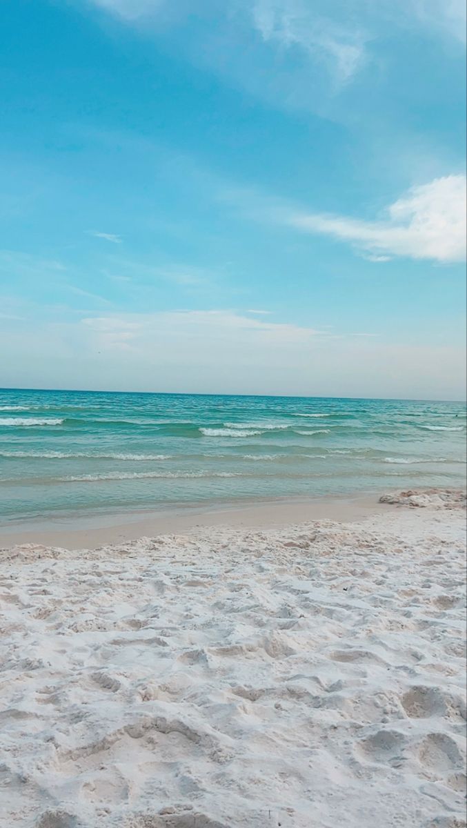 the surfboard is laying on the beach in front of the ocean and blue sky