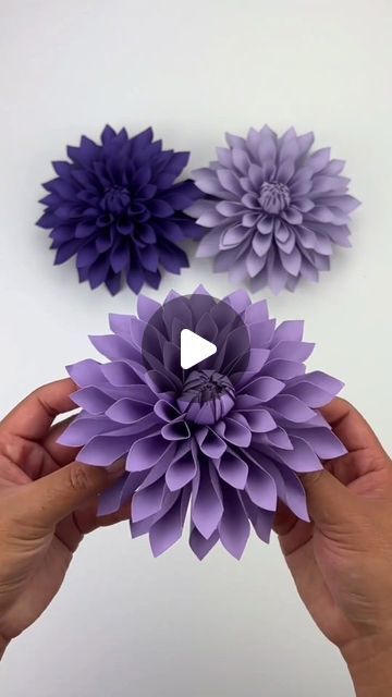 two purple paper flowers being held by someone's hands