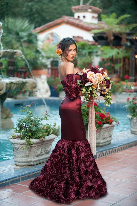 a woman in a long dress holding a bouquet next to a fountain with flowers on it