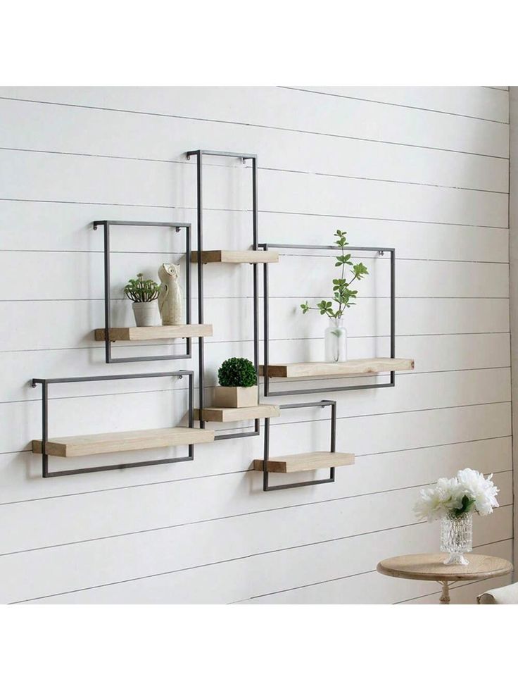 three shelves with plants and vases on them against a white wall in a living room