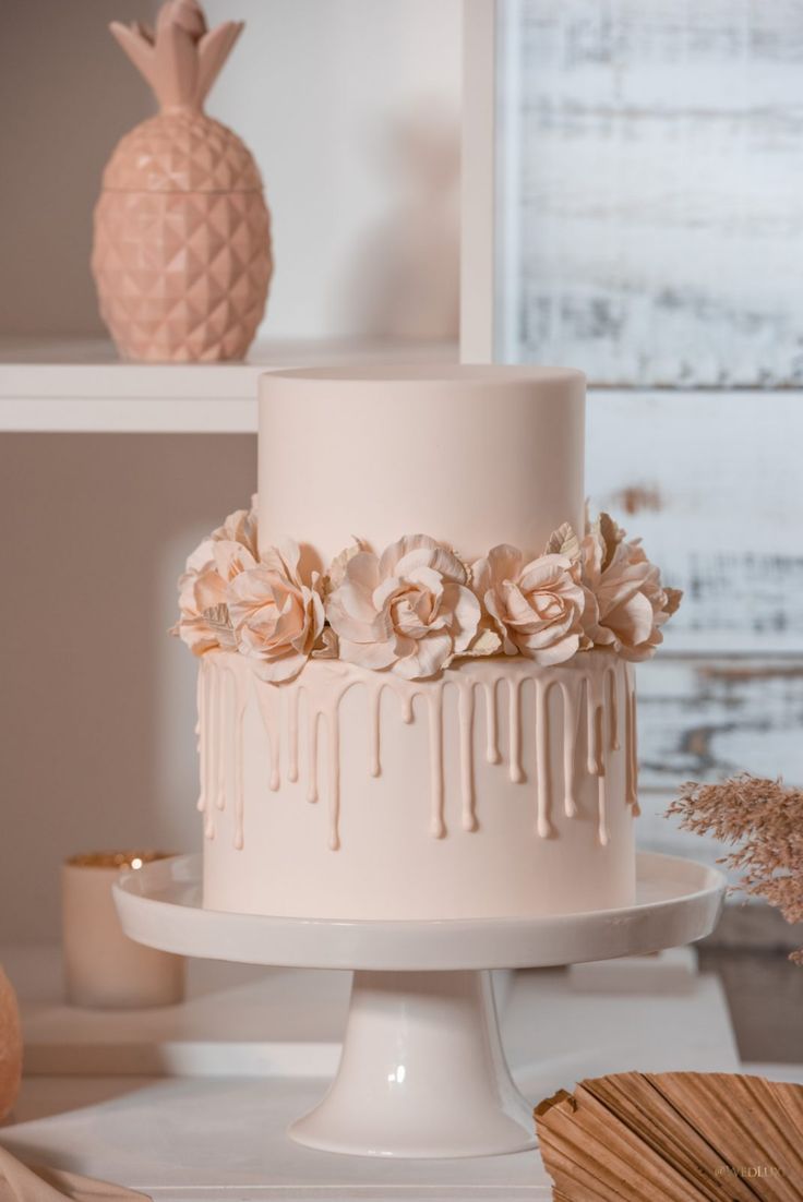 a three tiered cake with flowers and dripping icing on the top is sitting on a table